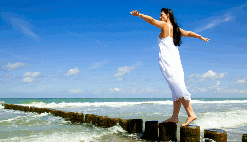 A woman balances on a set of concrete pier posts that extend into the ocean