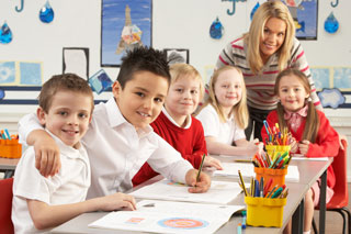 A group of primary schoolchildren and their teacher working at desks in a classroom