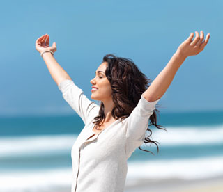A woman standing on the beach with arms outstretched above