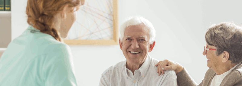 An elderly man and woman smiling and talking to a woman