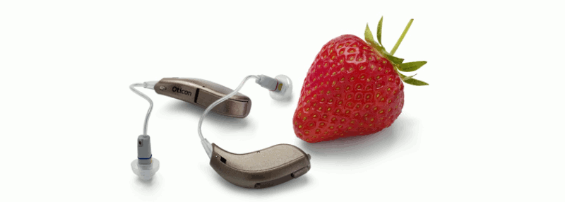 A pair of RITE open dome hearing aids beside a strawberry