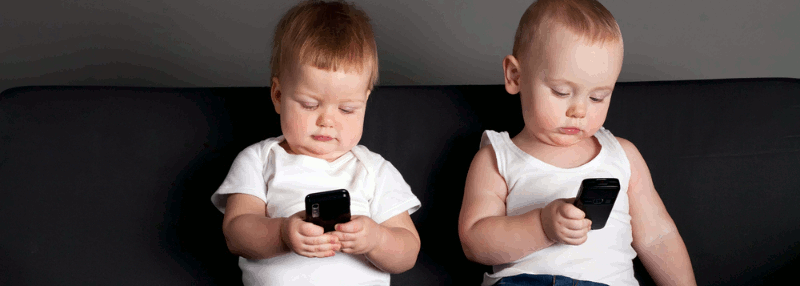 Two babies on a couch playing with mobile phones