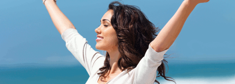 A woman standing on the beach with arms outstretched above